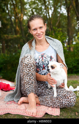 Une femme blanche avec les cheveux bruns se reposant dans un parc, son chien assis sur le tapis barefoot Banque D'Images