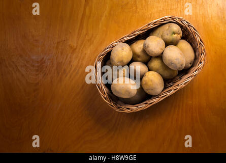 Les pommes de terre en panier en osier sur le comptoir en bois Banque D'Images