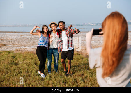 Jeune femme rousse prendre des photos de ses amis avec un téléphone mobile à l'extérieur Banque D'Images