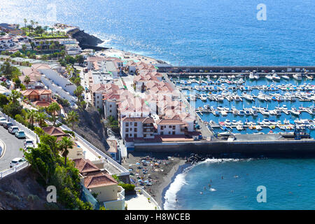 Vue aérienne ville côtière de Los Gigantes à Ténérife, avec un petit bateau , port , plage de sable de couleur sombre hillside villas Banque D'Images