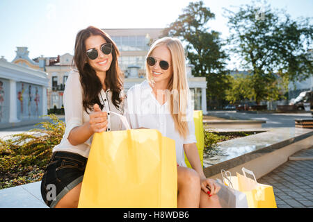 Deux belles jeunes filles à lunettes reposant sur banc après shopping Banque D'Images