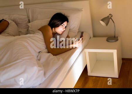 Jeune couple au lit. L'homme dort tandis qu'une jeune femme à la nuit au téléphone Banque D'Images