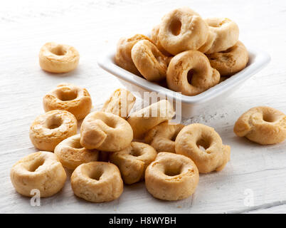Taralli italiens pour un délicieux craquelins collations doigt servi dans un petit bol de répandre dans un tas sur une planche de bois blanc Banque D'Images