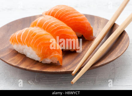 Vue rapprochée de trois sushis saumon frais Nighiri de tranches de filets de poissons sur les monticules de riz servi sur une plaque de bois Banque D'Images