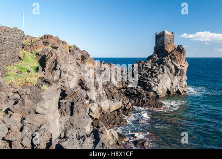 La côte rocheuse de la falaise de lave près de Taormina (Sicile), avec un tour de garde dans l'arrière-plan Banque D'Images