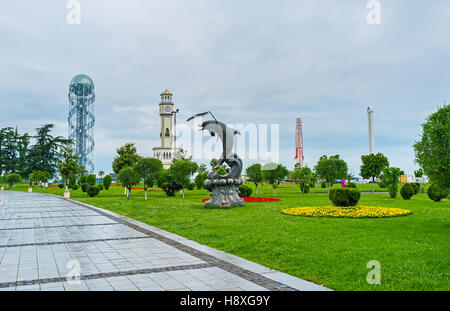 La statue du dauphin dans la station jardin avec la tour de l'horloge et la grande roue sur l'arrière-plan, Batumi, Géorgie. Banque D'Images