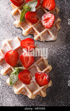 Gaufres Belges avec des fraises fraîches, du sucre en poudre et la menthe close-up sur la table. vertical Vue de dessus Banque D'Images