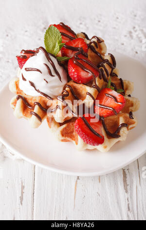 Gaufres Belges avec des fraises, de la crème fouettée et de chocolat sur une plaque verticale. Banque D'Images