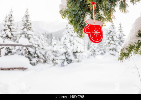 Ornements de Noël jouets en bois mitten avec ruban accroché à un arbre avec de la neige. Banque D'Images