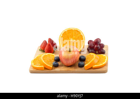 Les raisins rouges avec une demi-orange et coupes, fraises, bleuets et apple sur planche de bois isolé sur fond blanc Banque D'Images