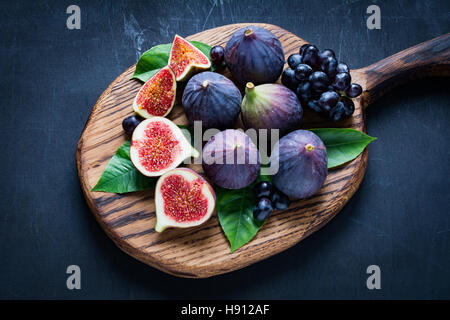 Plateau à fruits : figues fraîches et les raisins noirs 'Isabella' sur planche à découper en bois. Vue horizontale Banque D'Images