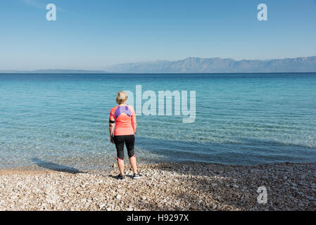 Une femme vêtue de course se dresse sur une plage dos à la caméra à la recherche à travers la mer Adriatique en Croatie lors d'une journée ensoleillée Banque D'Images