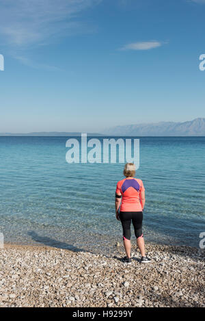 Une femme vêtue de course se dresse sur une plage dos à la caméra à la recherche à travers la mer Adriatique en Croatie lors d'une journée ensoleillée Banque D'Images