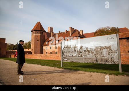 Homme debout à l'extérieur le château de Malbork Pologne regarder une affiche montrant les destructions causées pendant la seconde guerre mondiale Banque D'Images