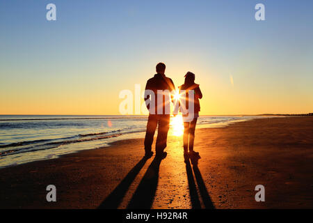 Les silhouettes d'un père et sa fille à pied sur la plage pendant le coucher du soleil se tenant la main. Banque D'Images