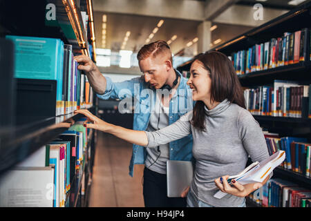 Deux jeunes étudiants obtenant des livres sur une étagère de bibliothèque publique. étudiants universitaires à la bibliothèque à la recherche d'informations pour leurs études. Banque D'Images