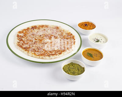 L'uthappam à l'oignon dans une assiette servie avec sambar et trois types de chutneys est un tiffin traditionnel de l'Inde du Sud sur fond blanc Banque D'Images