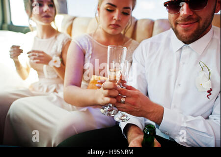Groomsman élégant ou Meilleur homme du marié et de demoiselles d'intérieur à limousine mariage verse dans des verres de champagne. Banque D'Images