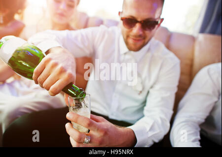 Groomsman élégant ou Meilleur homme du marié et de demoiselles d'intérieur à limousine mariage verse dans des verres de champagne. Banque D'Images