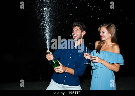 Cheerful young couple bouteille de champagne et s'amuser dans la nuit Banque D'Images