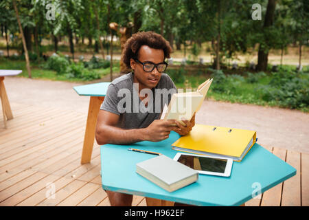 L'Afrique concentre jeune homme assis et reading book outdoors Banque D'Images