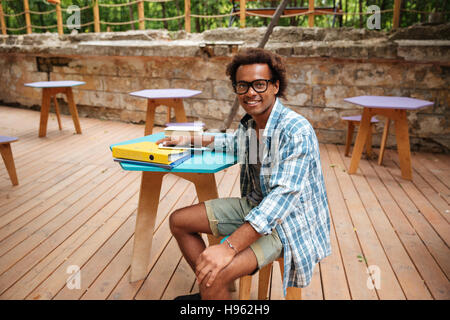 Cheerful young African man dans les verres et chemise à carreaux assis en terrasse d'un café Banque D'Images