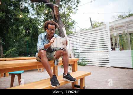 Beau jeune homme afro-américain dans les verres avec tablet sitting in park Banque D'Images