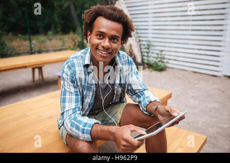 L'Afrique de l'heureux jeune homme assis et écouter de la musique à partir de la tablet Banque D'Images