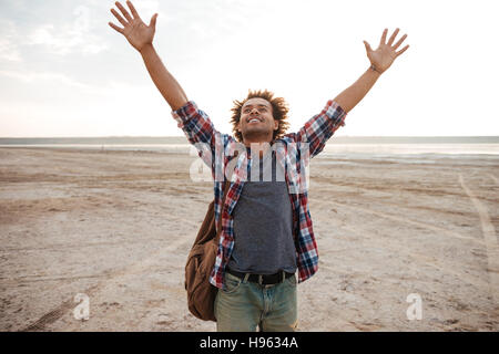Heureux jeune homme africain attrayant avec main levée debout sur la plage Banque D'Images