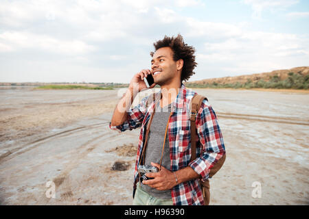 Jeune homme africain gai avec old vintage photo caméra et permanent talking on cell phone Banque D'Images