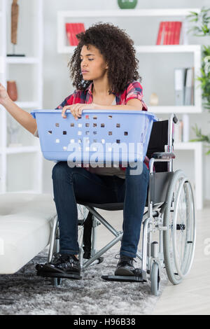 Jeune femme en fauteuil roulant à mettre dans la machine à laver blanchisserie Banque D'Images