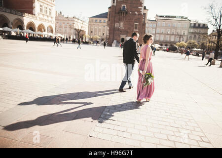 Mariage. beau couple, mariée avec robe rose marche dans la vieille ville de Cracovie, leurs ombres Banque D'Images