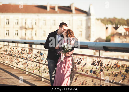 Couple de mariage amour élégant, groom, mariée avec robe rose embrasser et s'étreindre sur un pont au coucher du soleil Banque D'Images
