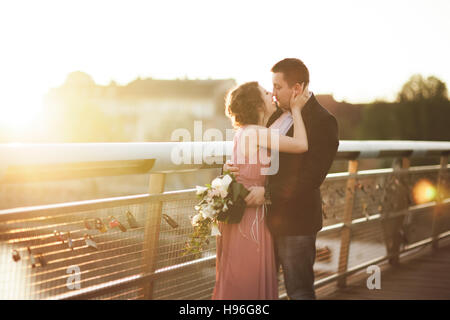 Couple de mariage amour élégant, groom, mariée avec robe rose embrasser et s'étreindre sur un pont au coucher du soleil Banque D'Images