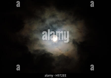 Lune brille à travers les nuages colorés sur une nuit sombre. Banque D'Images