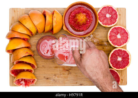 Man pouring ruby fraîchement pressé jus de pamplemousse riche en pectine soluble fibre d'une cruche dans un verre sur une planche à découper en bambou avec une bordure de fre Banque D'Images