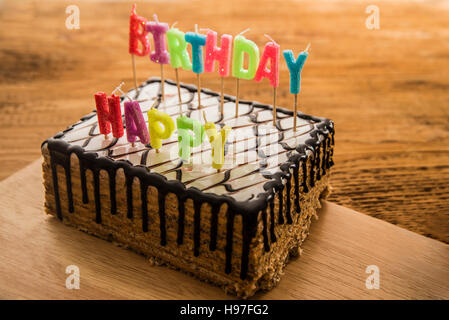 Joyeux anniversaire bougies sur un gâteau au chocolat blanc contre fond de bois Banque D'Images