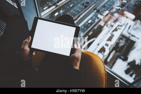 Vue rapprochée de la maquette du modèle de tablet pc dans les mains de l'homme assis près de la fenêtre de gratte-ciel, à l'aide de tablette numérique avec écran vide pour votre texte Banque D'Images