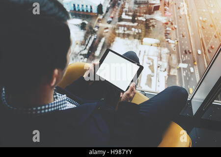 Maquette de modèle de tablet pc dans les mains de l'homme assis près de gratte-ciel de la fenêtre et à l'aide de tablette numérique moderne avec écran vide Banque D'Images