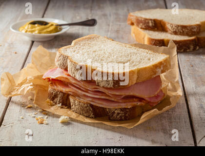 Un sandwich à la viande fumée sur une table en bois avec la moutarde. Banque D'Images