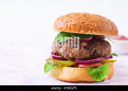 Big sandwich - hamburger burger de boeuf, cornichons, tomates et oignons rouges sur un fond clair. Banque D'Images