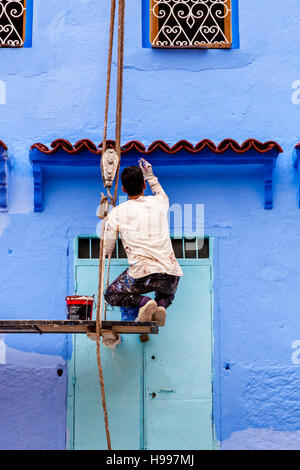 Un homme peint l'extérieur d'une maison traditionnelle en bleu, la médina, Chefchaouen, Maroc Banque D'Images