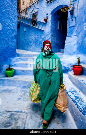 Une vieille femme marche dans les rues colorées de la Médina avec des sacs lourds, Chefchaouen, Maroc Banque D'Images