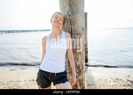 Young woman leaning against wooden post on beach Banque D'Images