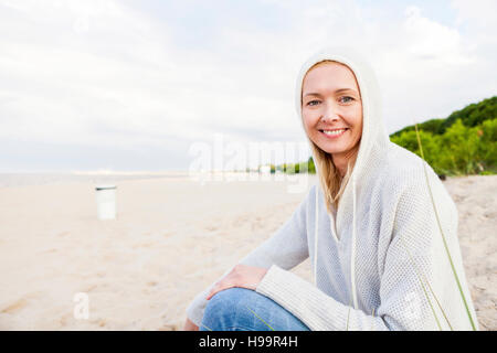 Femme avec hooded shirt assis sur une plage de sable Banque D'Images