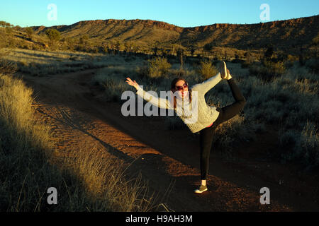 Une femme étend ses jambes et bras devant les MacDonnell Ranges, Alice Springs, territoire du Nord, Centre de l'Australie Banque D'Images