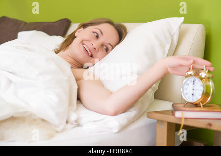 Jeune femme au lit, réveillé par son réveil Banque D'Images