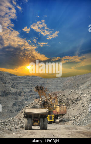 Les camions-benne lourd d'extraction sont chargés de minerai de fer sur les mines à ciel ouvert sur le coucher du soleil Banque D'Images