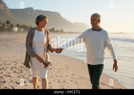 Shot de smiling mature couple sur la plage. Senior et senior woman holding hands et faire une promenade au bord de la mer. Banque D'Images