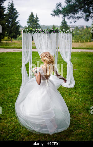 Belle blonde mariée dans une robe de mariée blanche tourne avec une robe à la main, robe en mouvement, n'a pas l'air dans l'appareil photo, Banque D'Images
